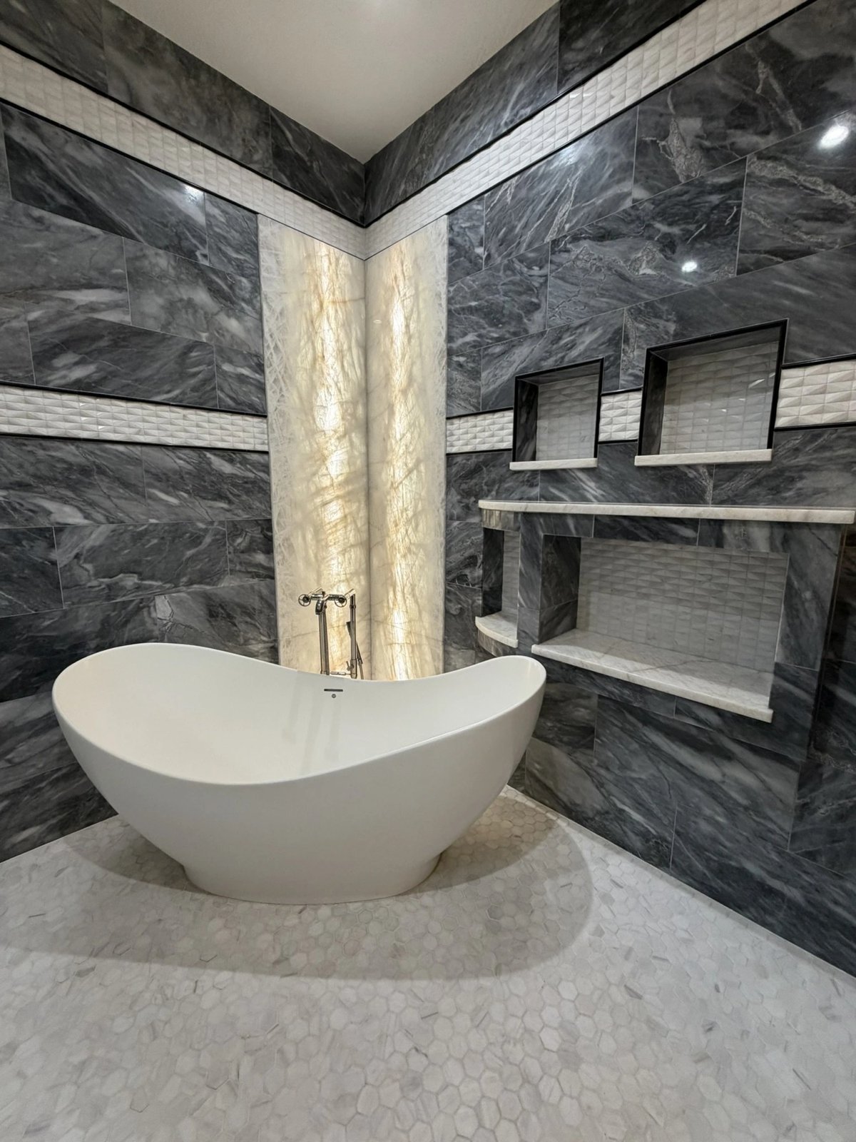 Primary bathroom with freestanding tub, backlit onyx column and marble walls, North Tampa custom home